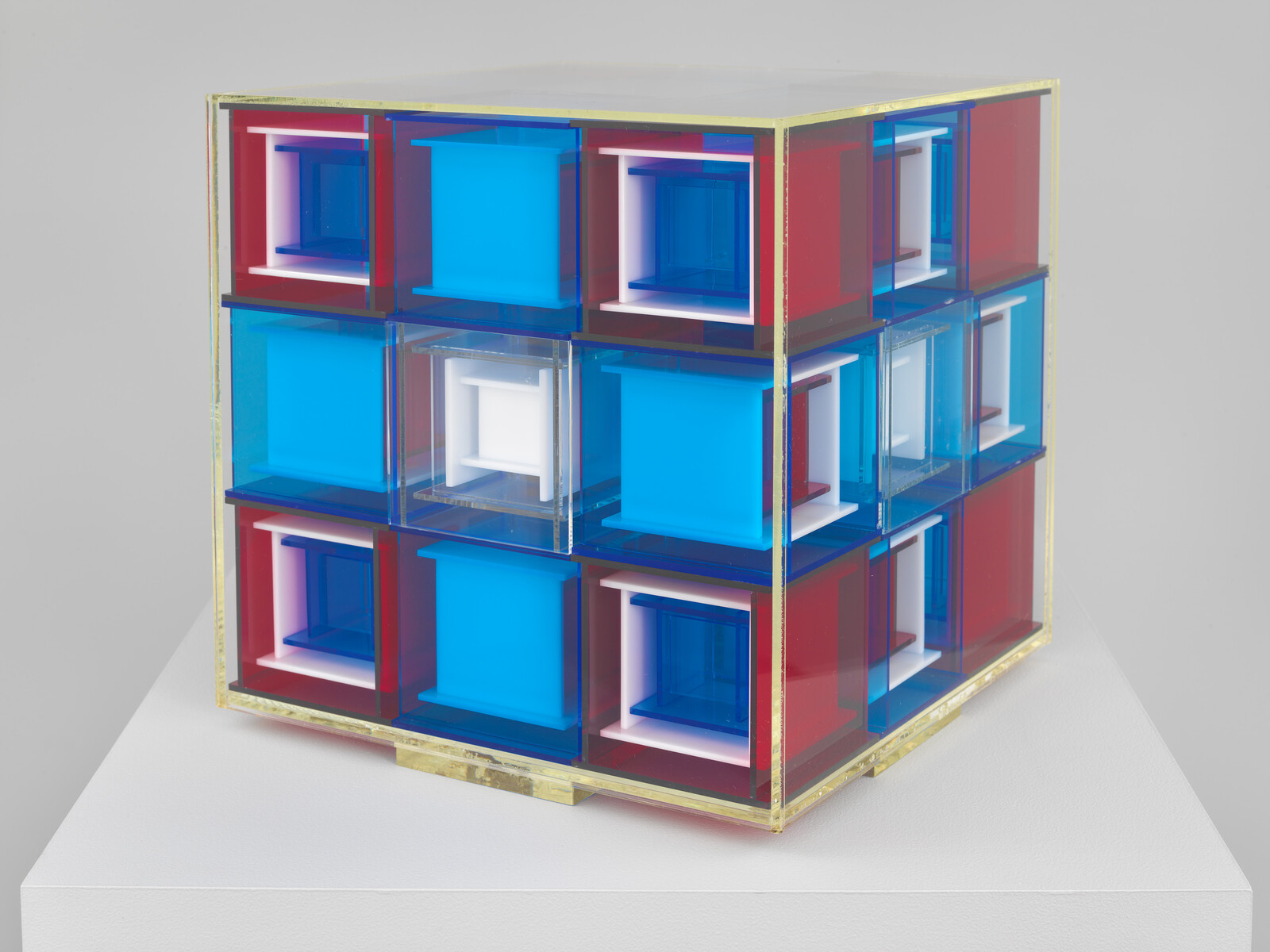 A transparent cube sculpture made of nested red, blue, and white smaller cubes on a pedestal.
