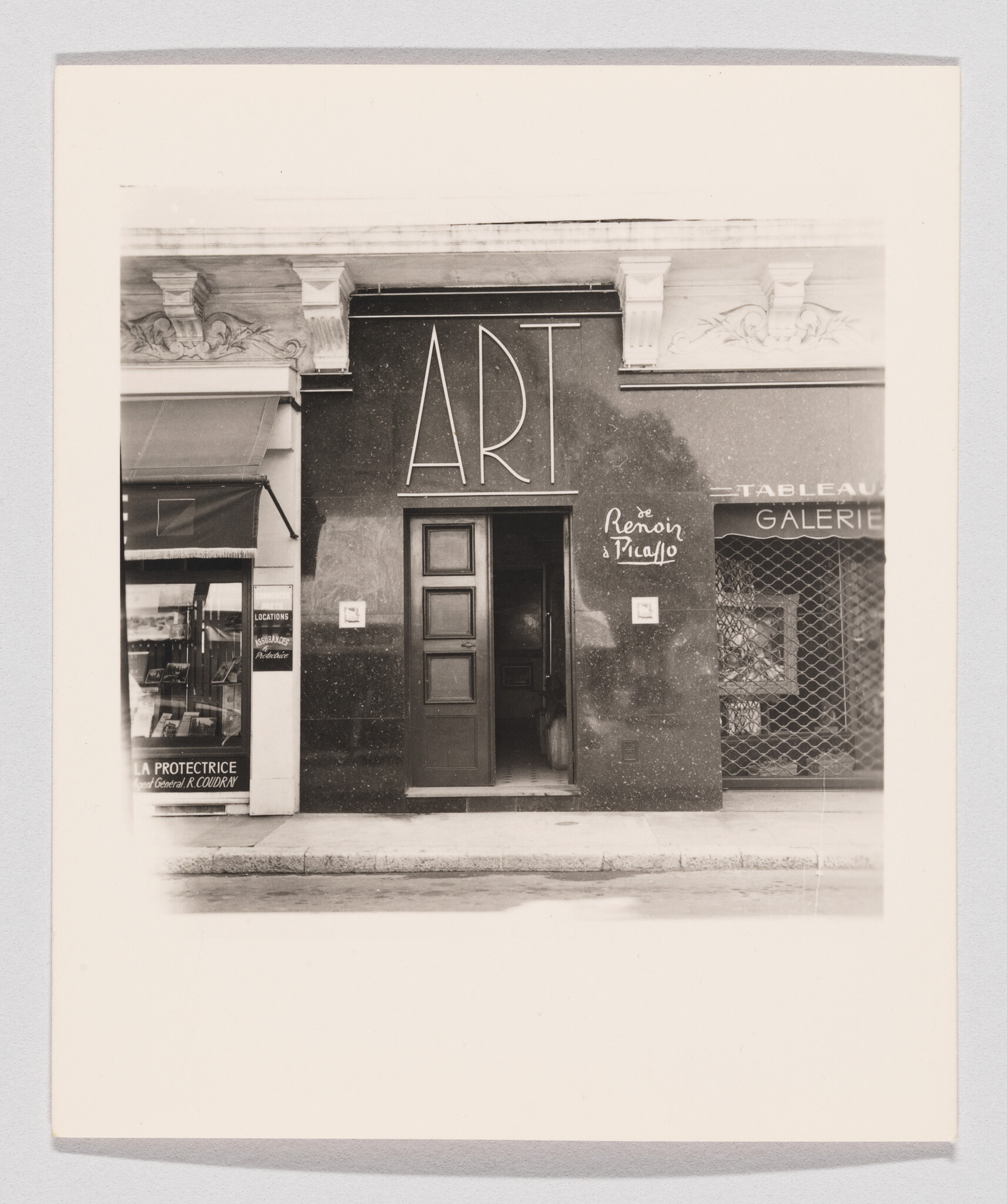 Gallery entrance with large ART sign above a central open door and adjacent shopfronts.