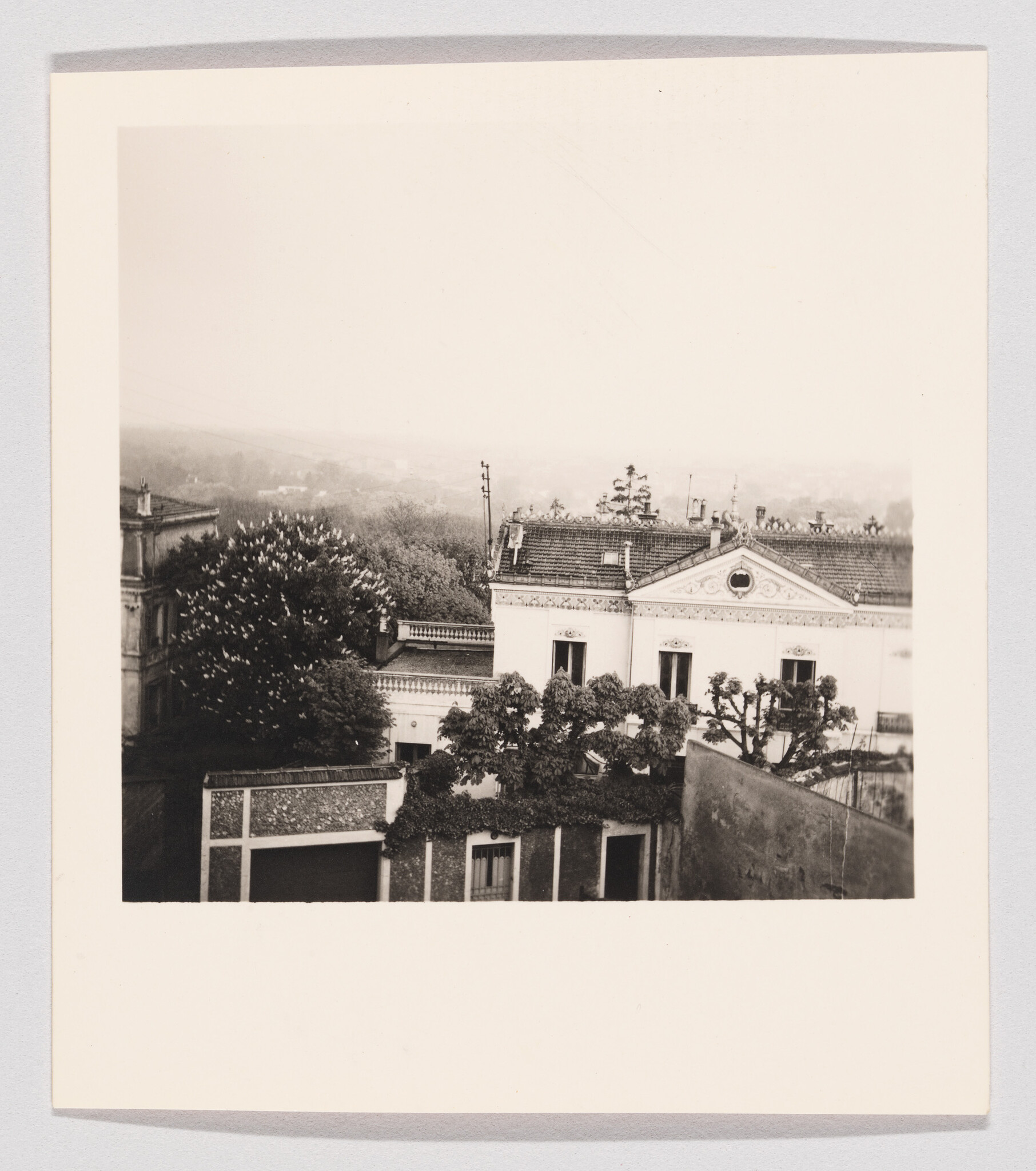 A vintage white villa with decorative roof and trees in the foreground under a hazy sky.