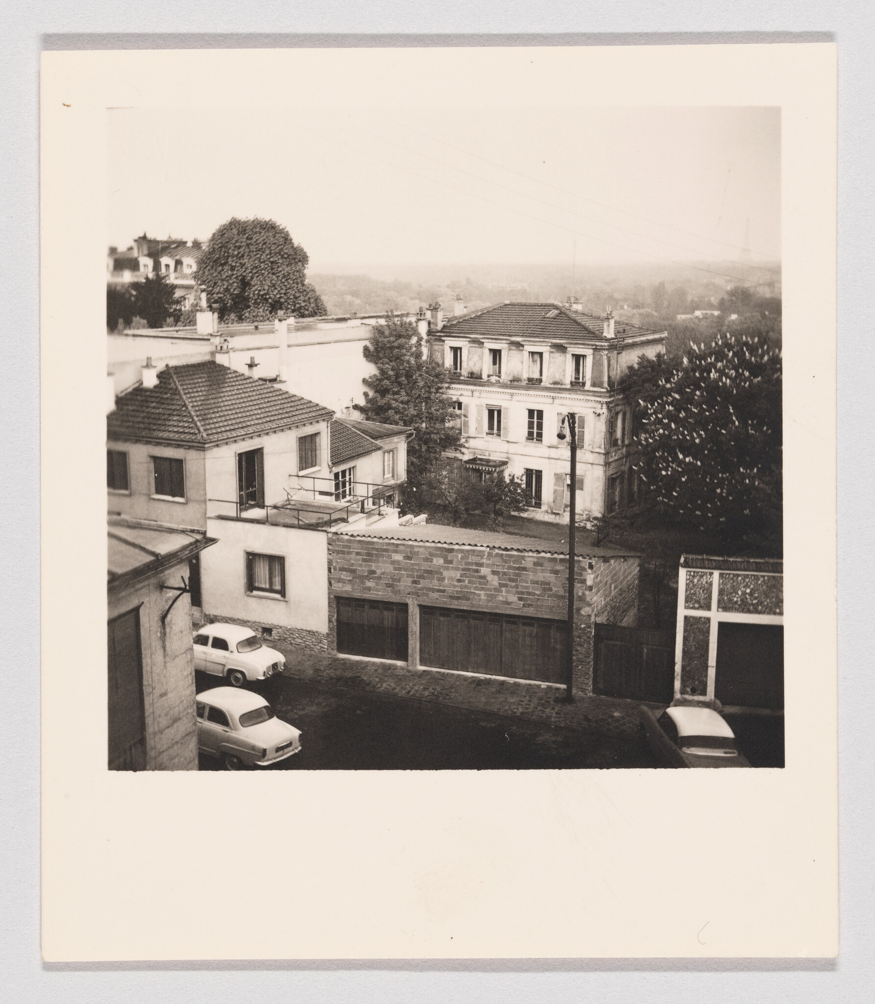Old residential buildings and garage row seen from above with three vintage cars parked nearby.