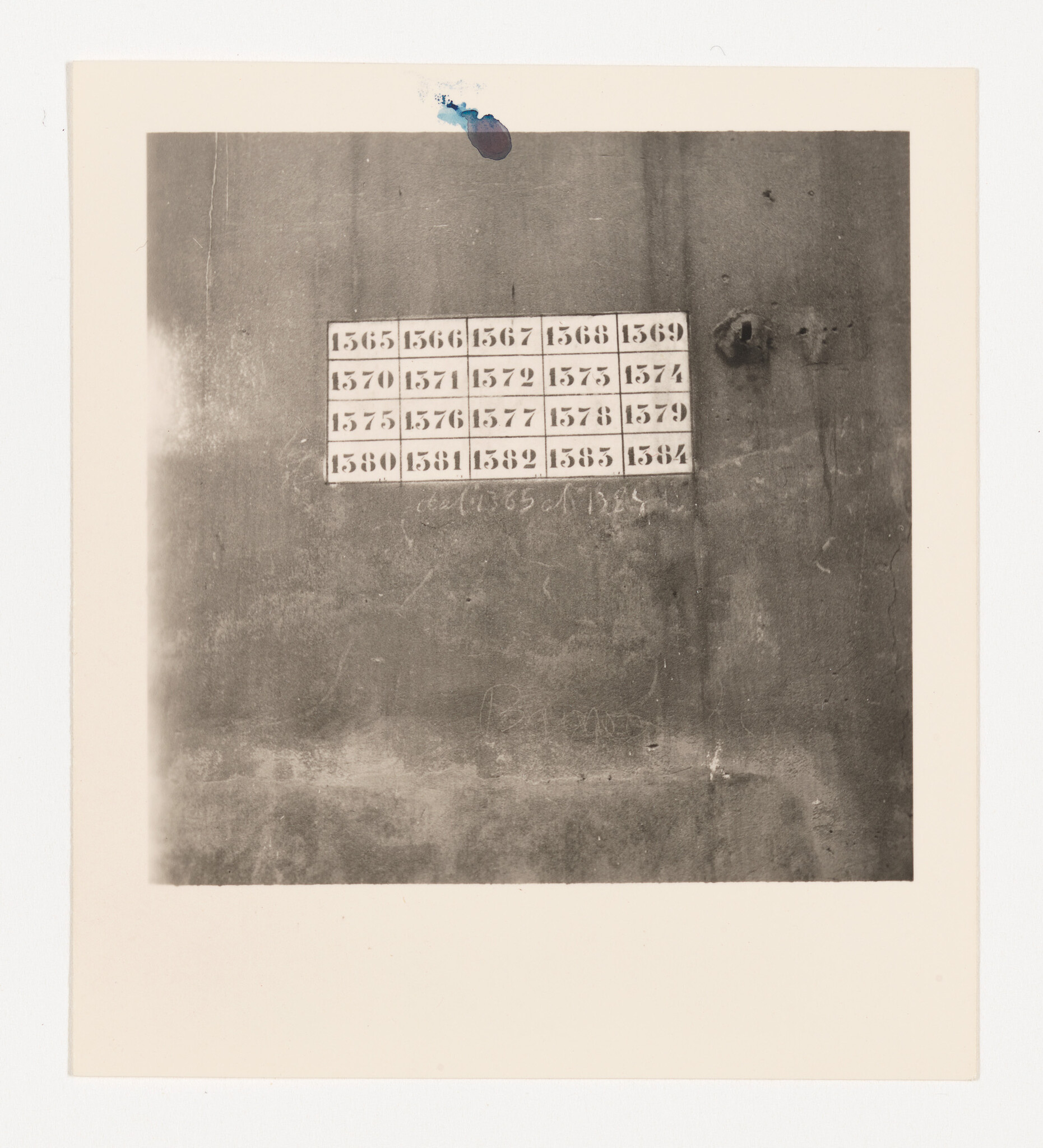 A faded wall with a grid of numbered paper tiles showing sequential numbers from 1565 to 1584.