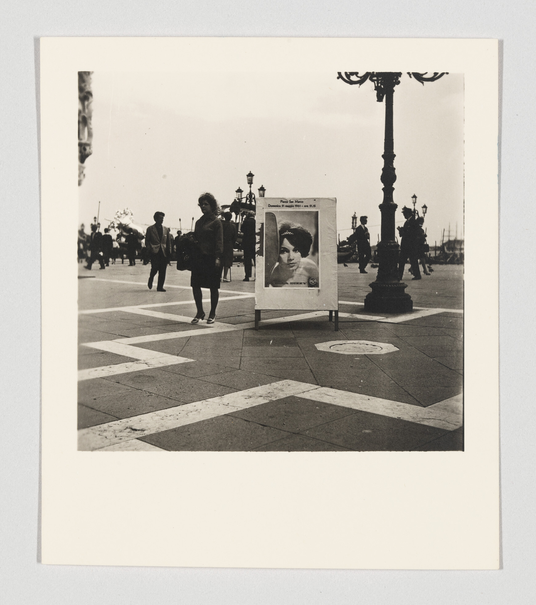 A woman walks past a freestanding poster of a woman's portrait in a busy plaza.