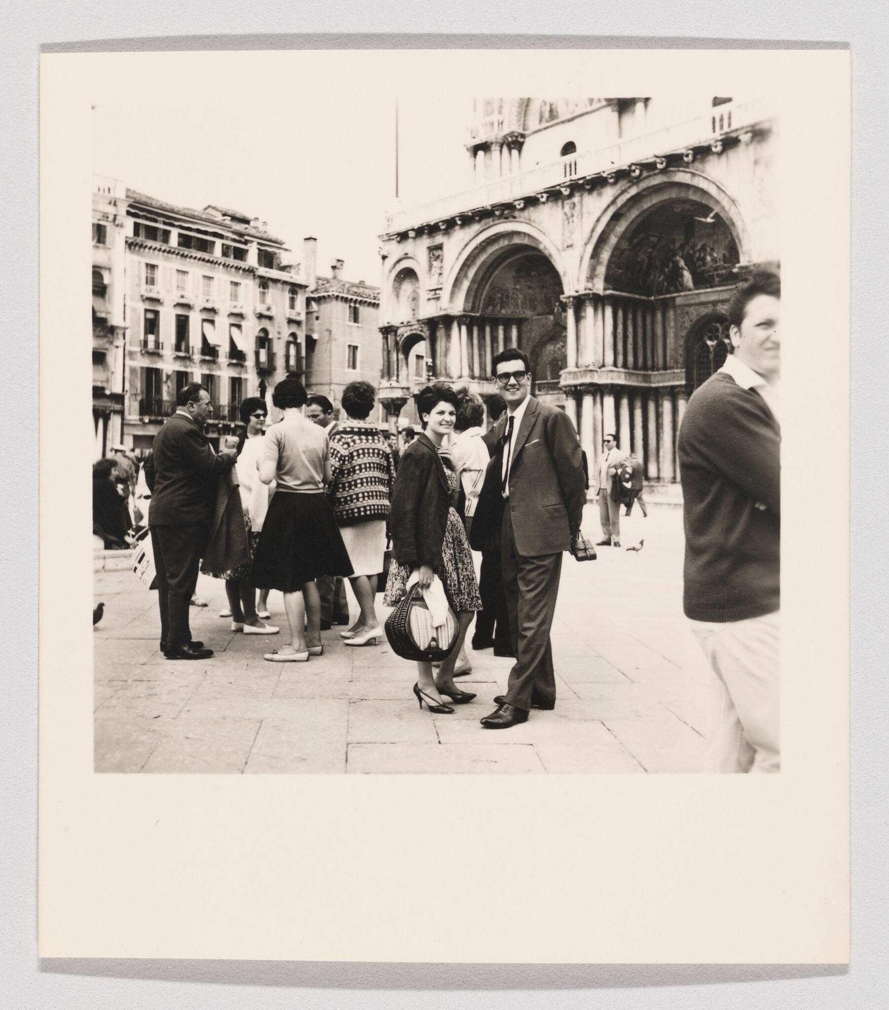 A smiling couple stands among tourists in front of a large ornate cathedral.