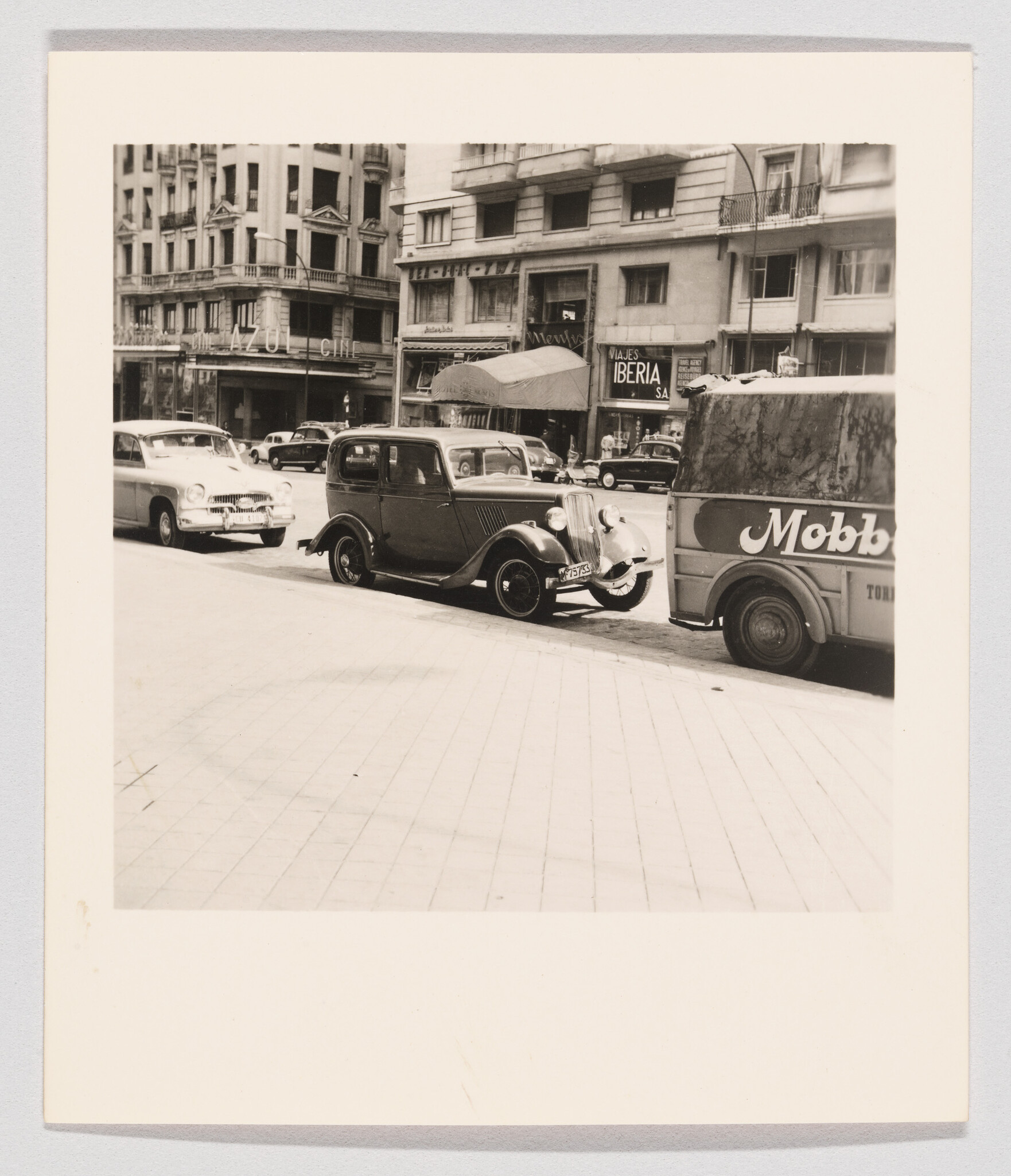 A vintage car is parked on a busy city street in front of shops.