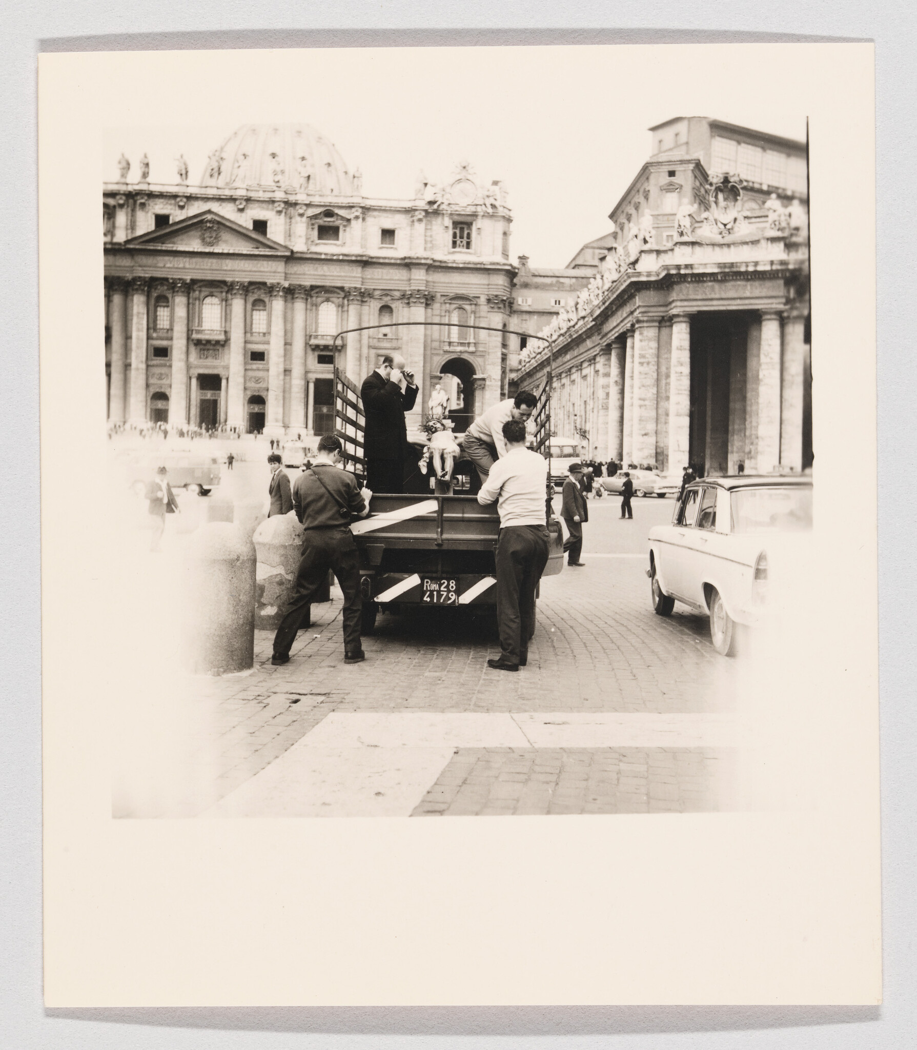 Workers lift a small religious statue onto a truck in front of St. Peter's Basilica.