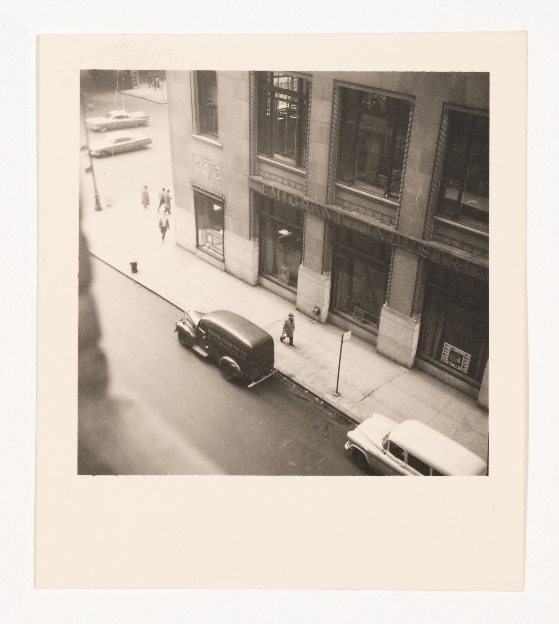 A delivery van is parked by a sidewalk while a person walks past an office building.