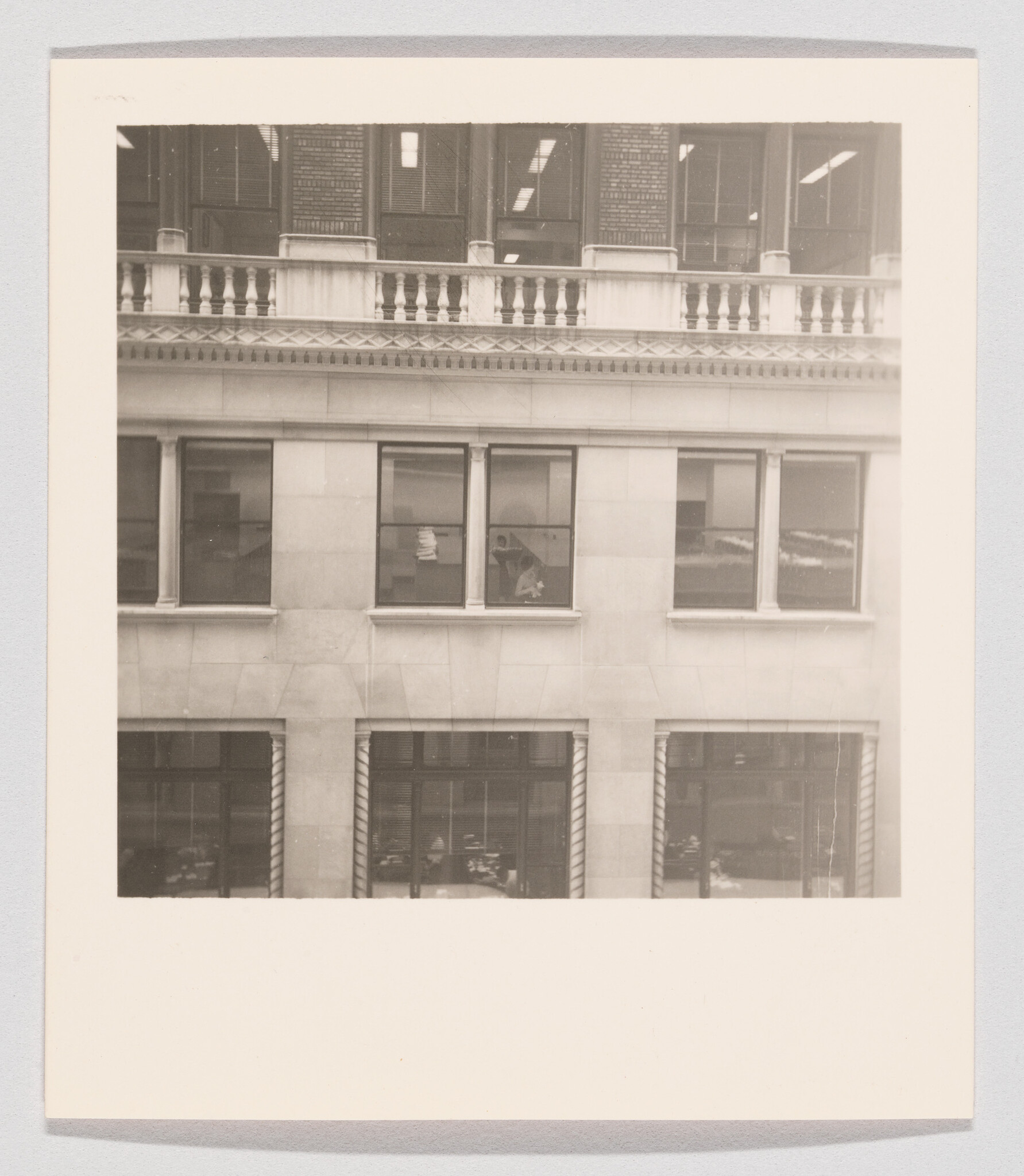Office building facade with a person leaning at a second-floor window holding papers.
