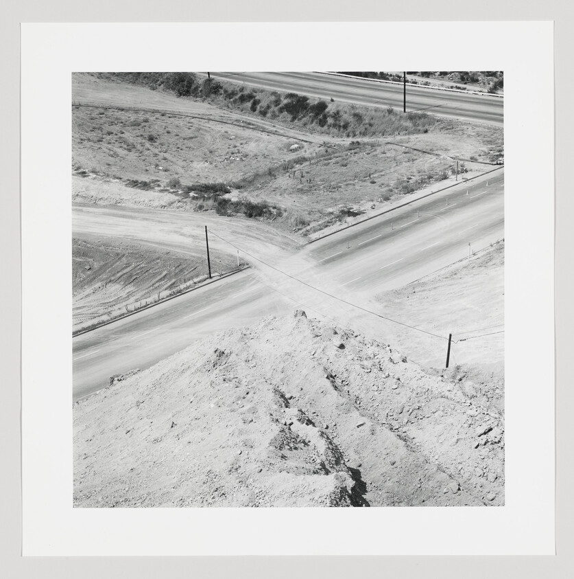 Aerial view of an empty four-way dirt intersection with a large dirt mound in the foreground.