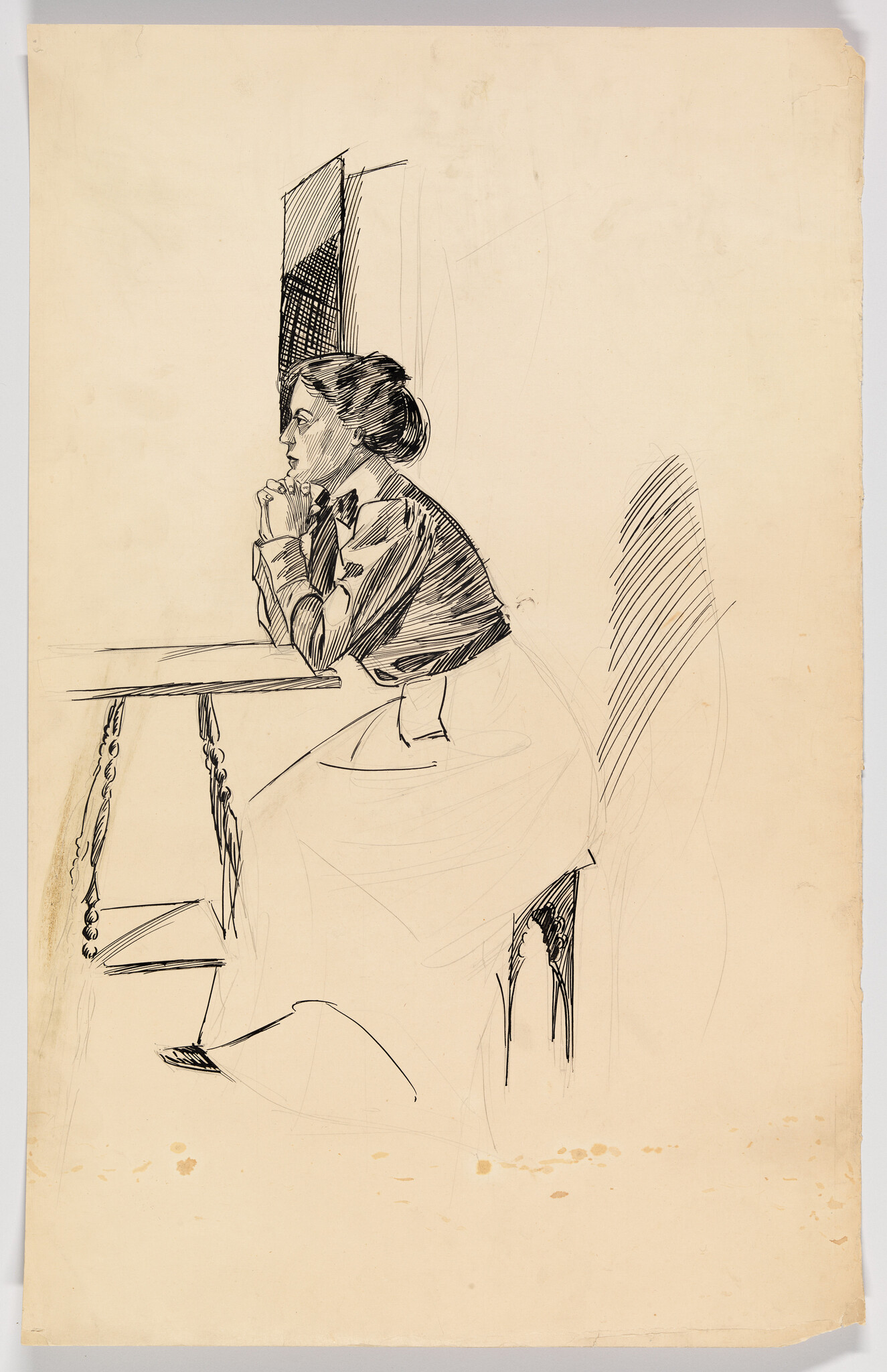 A woman sits at a table resting her chin on folded hands, looking thoughtfully forward.
