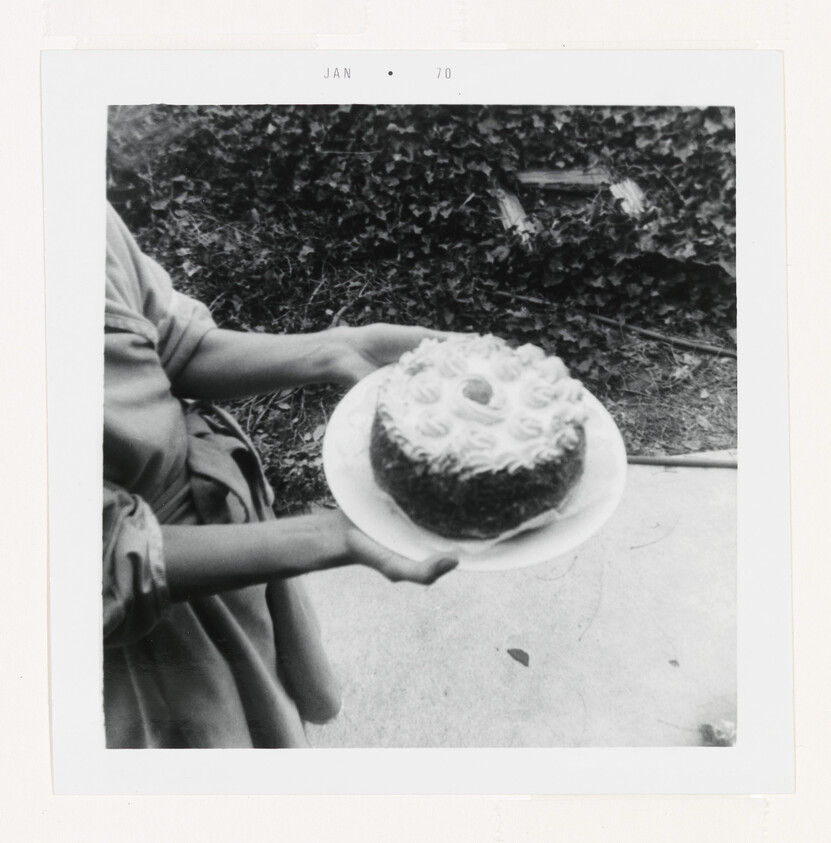 A person holds a decorated ring cake on a plate outdoors.