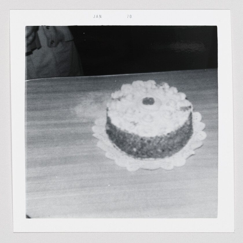 A round frosted cake sits on a paper doily on a wooden table.