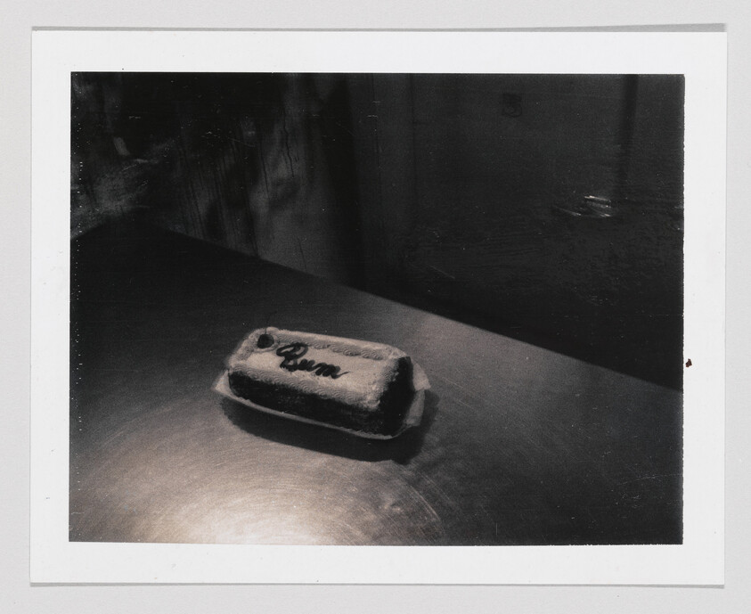 A small frosted loaf with the word "Queen" piped on top sits on a dark table.
