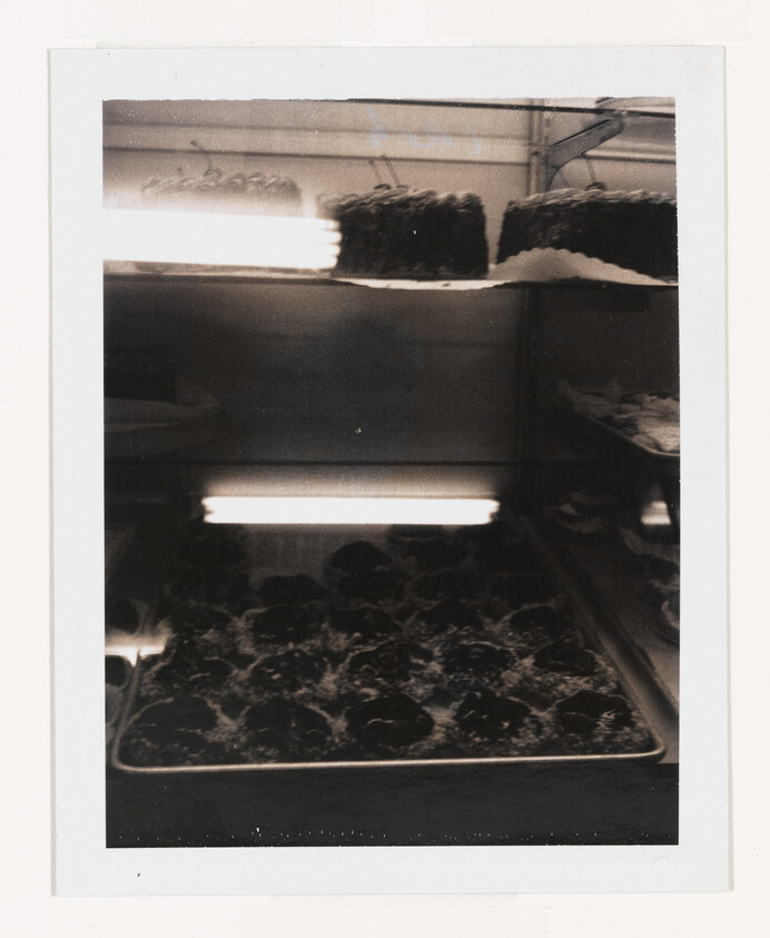 Tray of round pastries on a bakery display shelf with cakes on the top shelf.