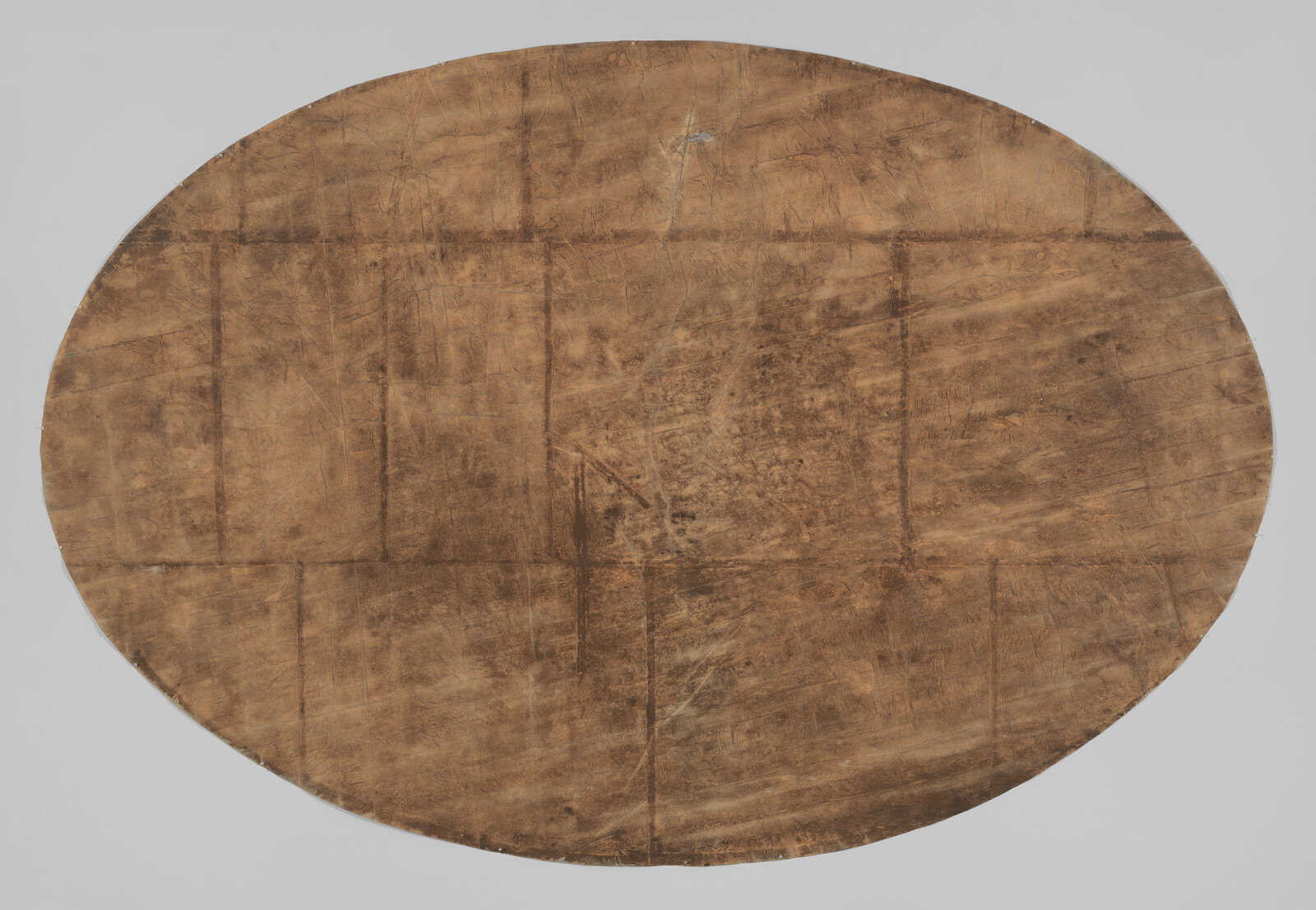 A large worn oval brown hide with visible seams, scratches, and scuff marks.