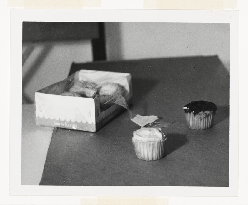 A box of cupcakes with two frosted cupcakes placed on a table nearby.