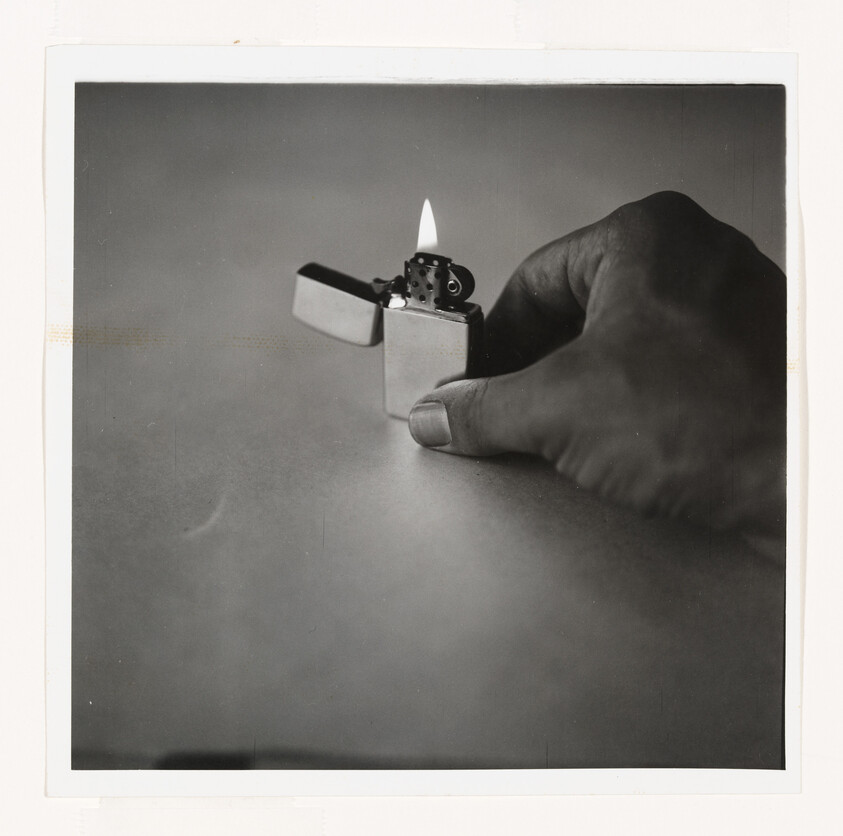 A hand holds a small metal flip-top lighter with a flame above the wick.