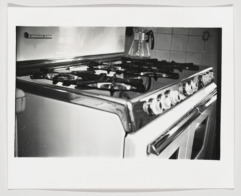 Vintage gas stove with four burner grates, row of control knobs, and a glass coffee pot.