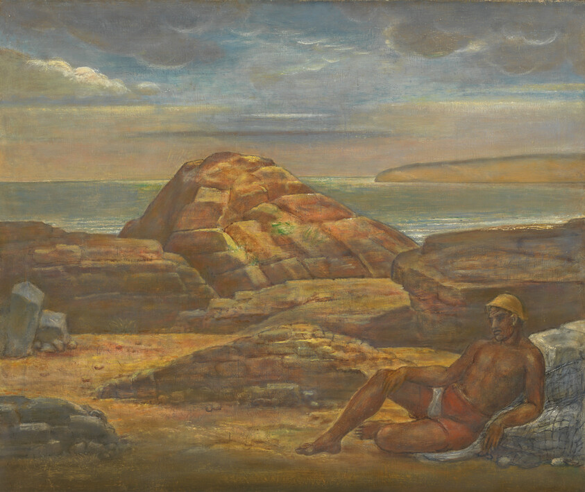 A shirtless man in a yellow hat rests on rocks by the sea at sunset.