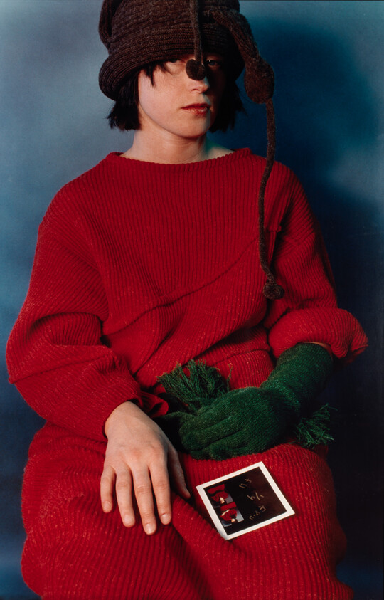 Child wearing a red sweater and green mittens sits holding a small photograph on their lap.