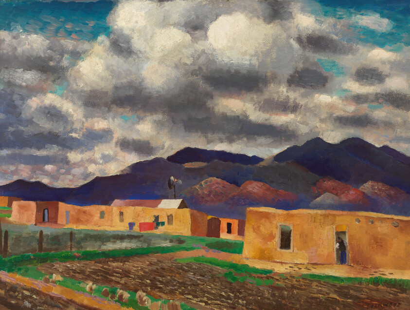 Adobe village with plowed fields in foreground, a person standing in a doorway and mountains under cloudy sky.