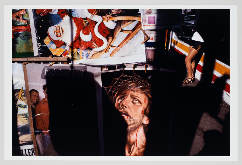 A painted depiction of Jesus with a crown of thorns displayed among colorful posters at a street stand.