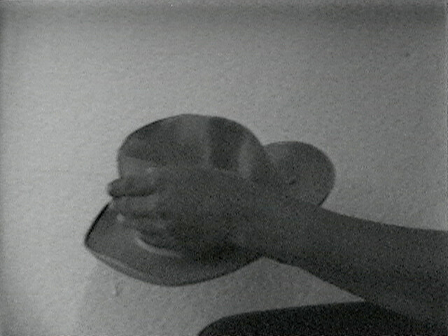 A person’s hand holding a cowboy hat against a plain wall, with the arm partially visible.