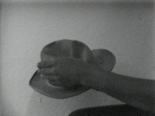 A pair of hands holds a metal bowl upside down over a shallow plate against a plain wall.