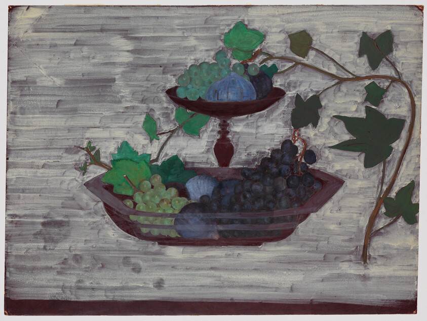A two-tiered bowl holding green and dark grapes with large vine leaves on a gray background.