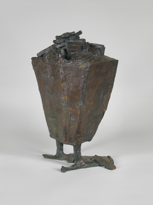 Bronze abstract sculpture resembling a tall box with rough surface standing on two bird-like legs.