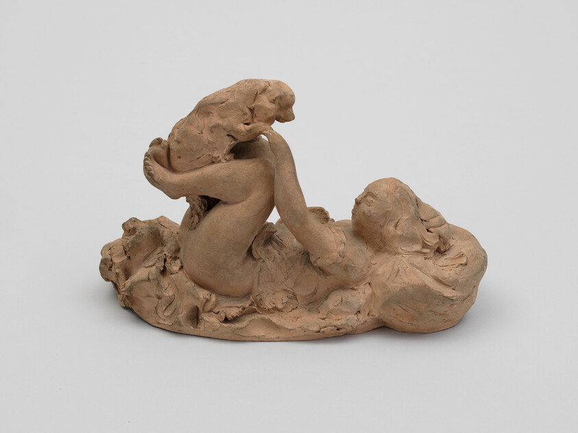A small terracotta sculpture of a reclining woman playfully lifting a dog above her bent knees.