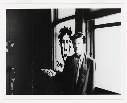 A person stands by a window pointing a small revolver beside a drawn face on the glass.