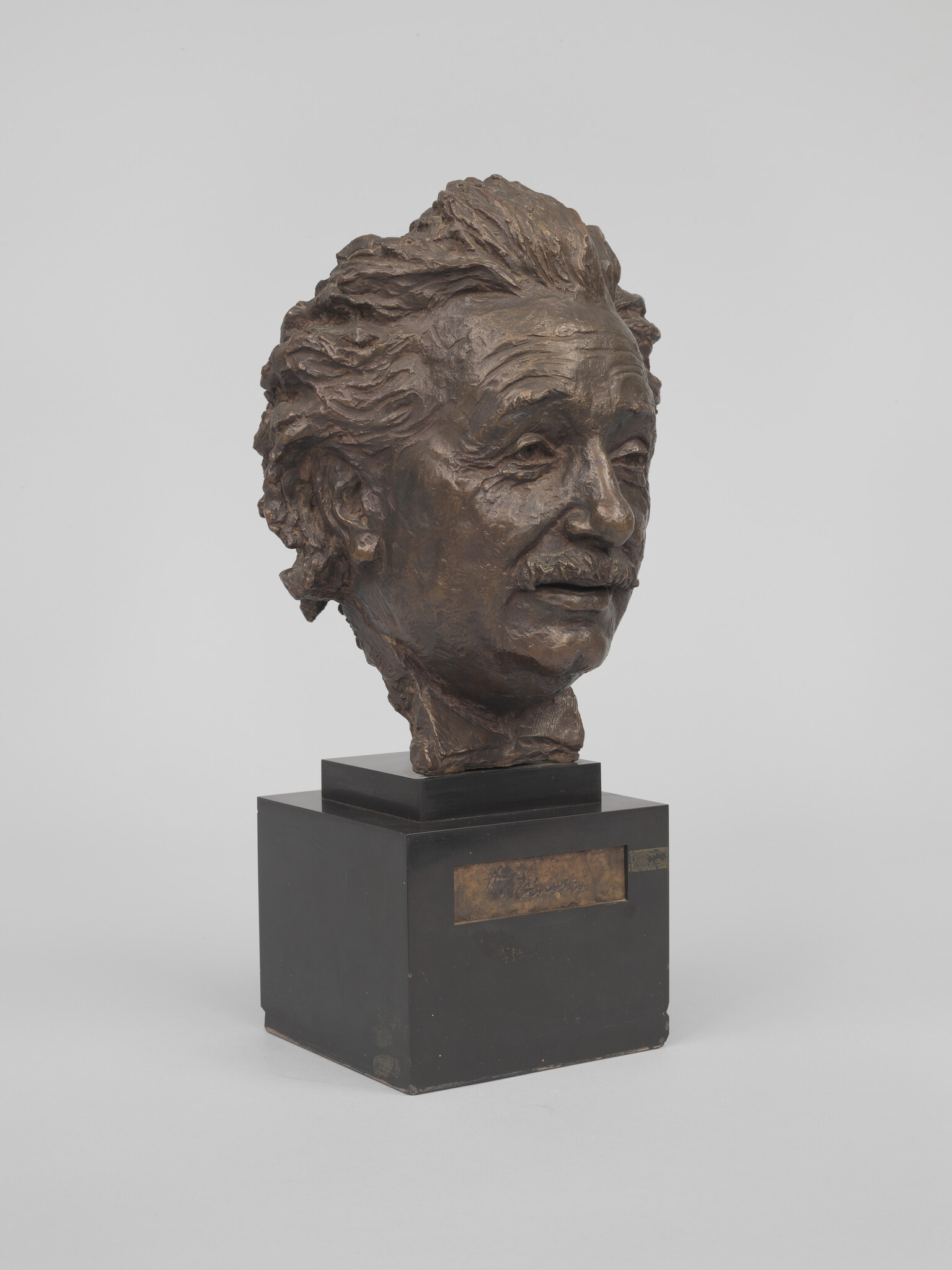 Bronze bust of an older man with tousled hair and a mustache mounted on a black pedestal.