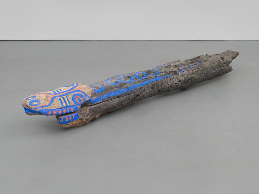A long charred wooden log painted with blue and orange abstract animal patterns lies on the floor.