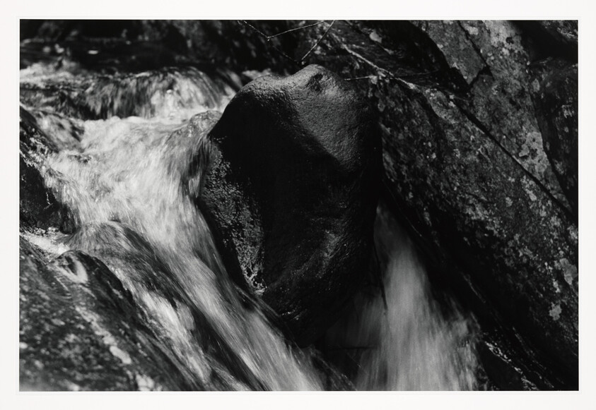 Water rushes through a narrow rocky channel around a large dark boulder, creating blurred motion.