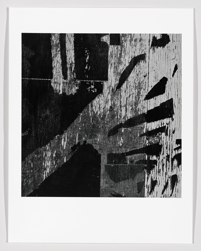 Abstract black-and-white print showing weathered wood grain and bold diagonal dark shapes.
