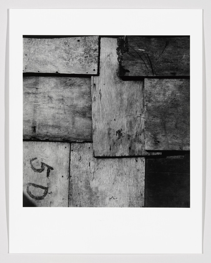 Weathered wooden planks overlapped in a grid pattern with a faded "5D" marking on one board.