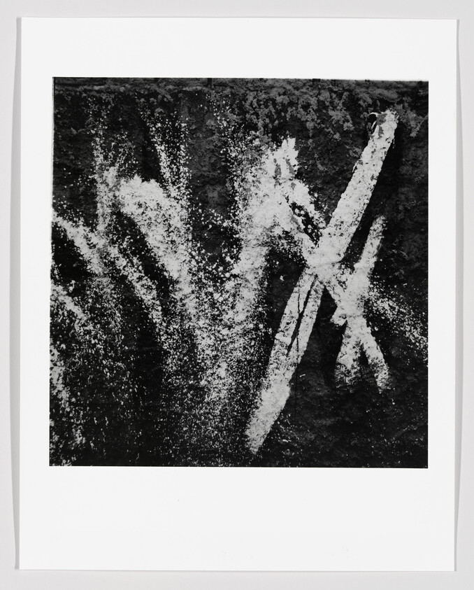 High-contrast black-and-white photograph showing white spray-like brush marks on a rough dark surface.