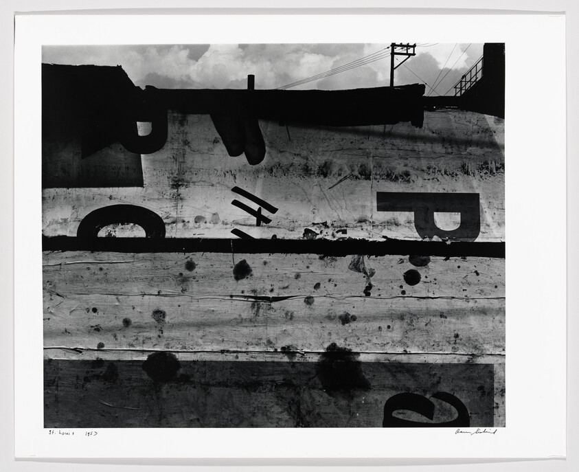 Weathered wooden billboard with large peeling letters and a distant utility pole against cloudy sky.