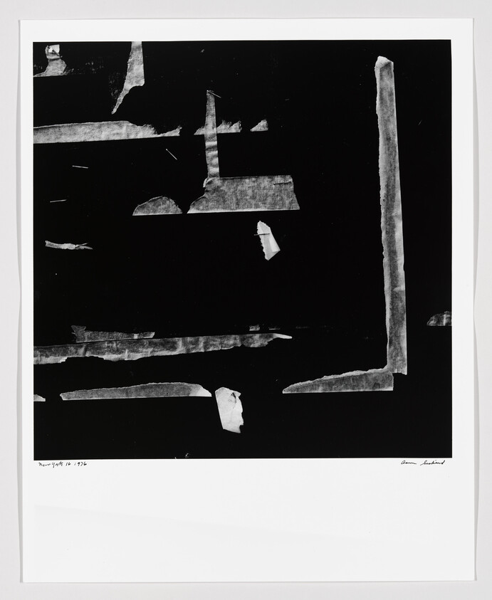 Black print showing torn white tape strips forming rough geometric shapes and scattered small fragments.