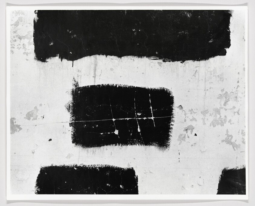 Three large black rectangular paint patches on a weathered white wall with cracks.