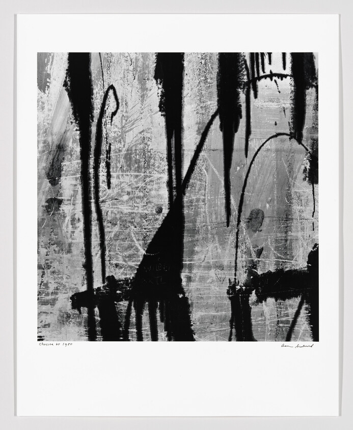 Abstract framed artwork showing black paint drips and scratches on a gray textured background.