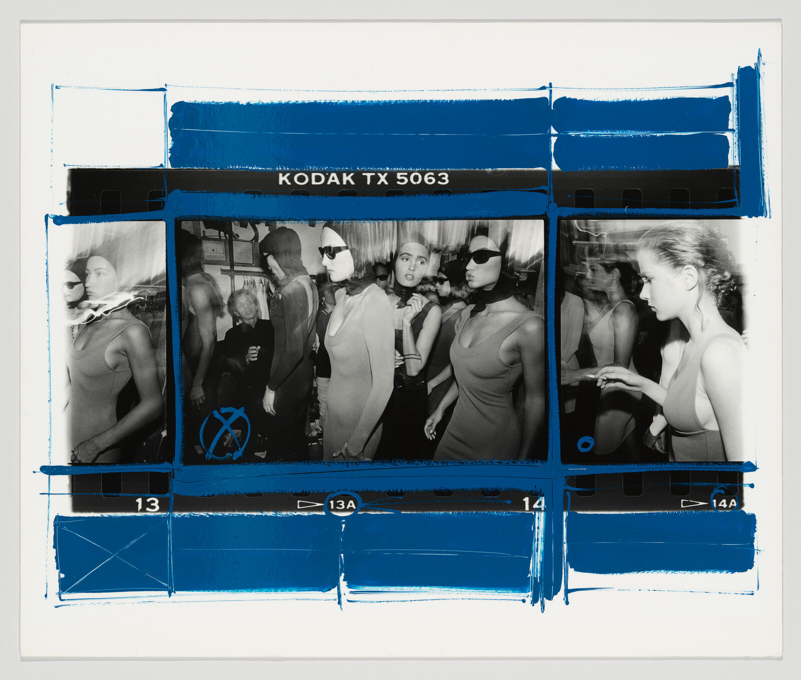 Models in fitted dresses and headscarves gather backstage, preparing and adjusting before a runway show.