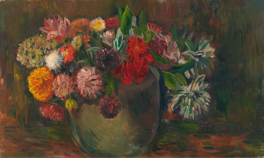A round ceramic vase holds a loose bouquet of colorful mixed flowers on a wooden table.