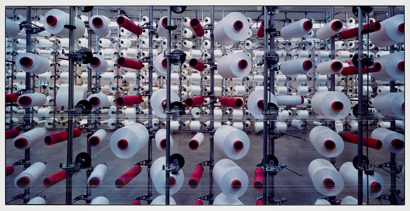 Rows of white and red thread spools on a textile machine in a factory.