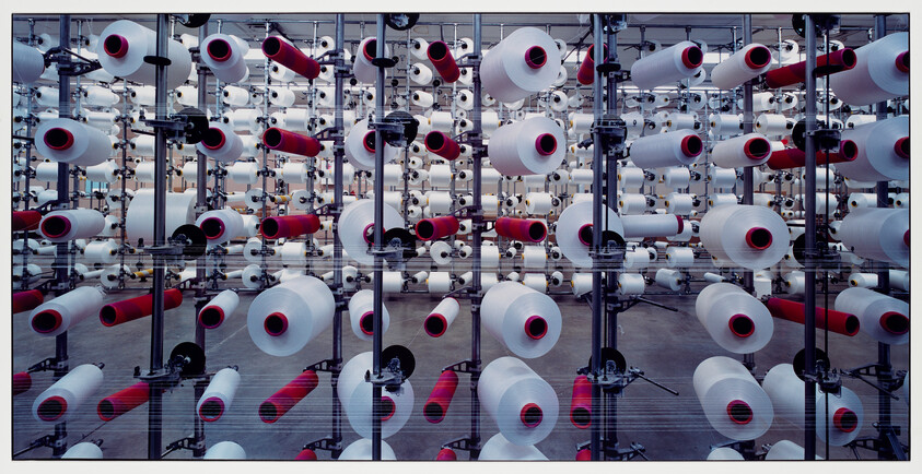 Rows of industrial yarn spools with red cores mounted on metal racks in a textile factory.