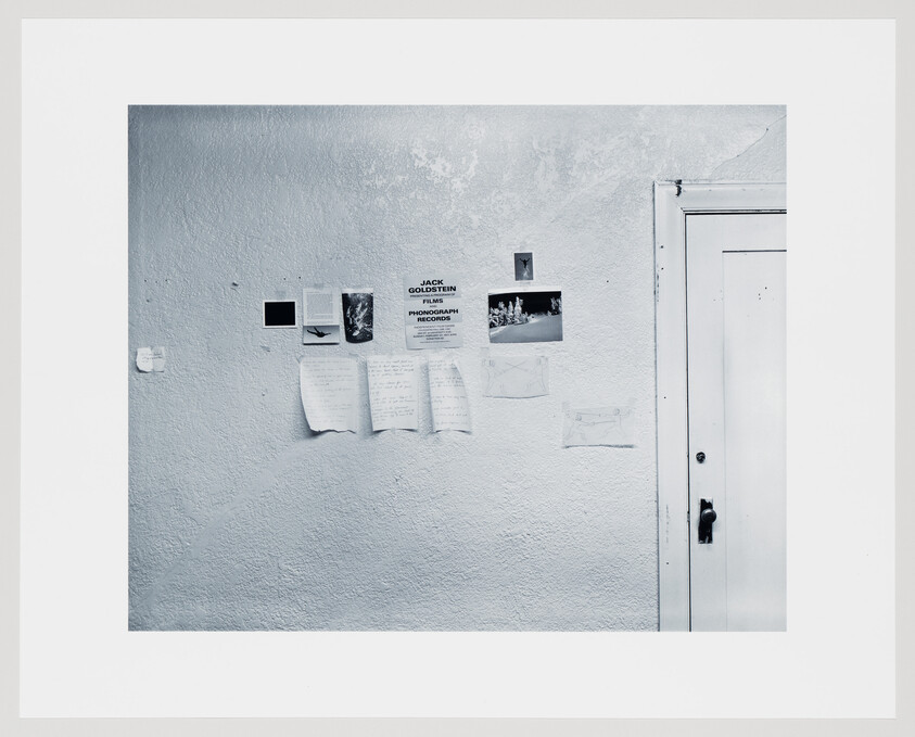 A textured white wall displays several taped photos and handwritten notes beside a closed white door.