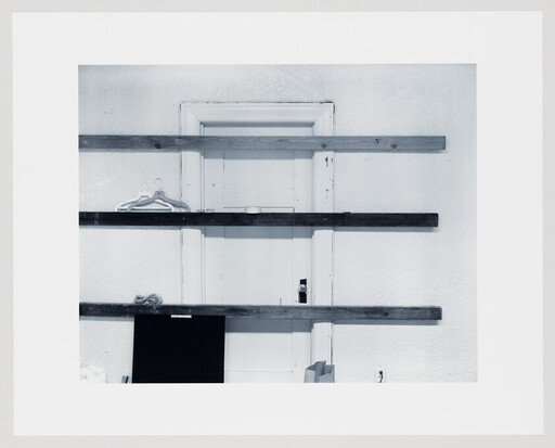 A white door is barred by three horizontal wooden planks with hangers and items nearby.