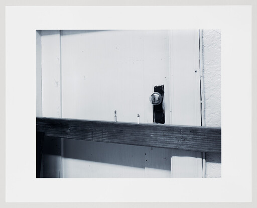 A white door is barricaded with a horizontal wooden plank nailed across near a round glass doorknob.