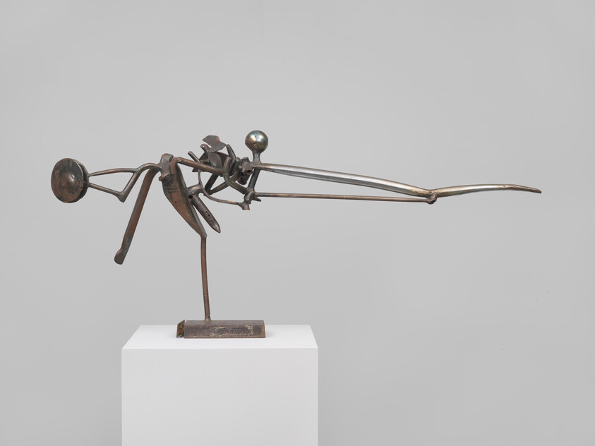 A bronze abstract sculpture on a pedestal with a long, thin beak-like projection and round head.