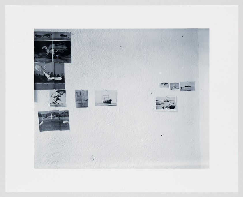 Small black-and-white postcards and photos arranged on a white textured wall.
